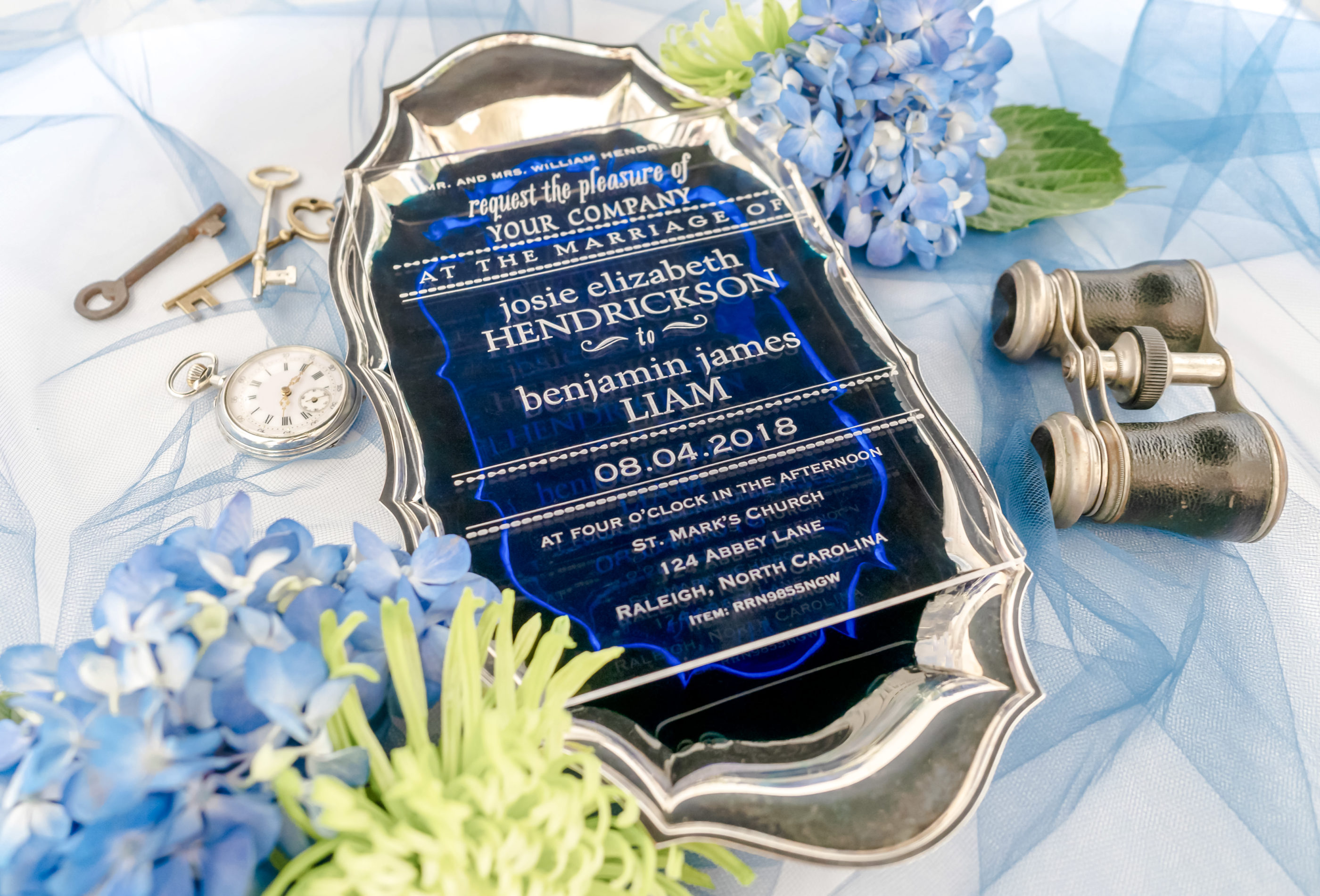 close photograph of clear acrylic invitation with white writing photographed on dark blue background