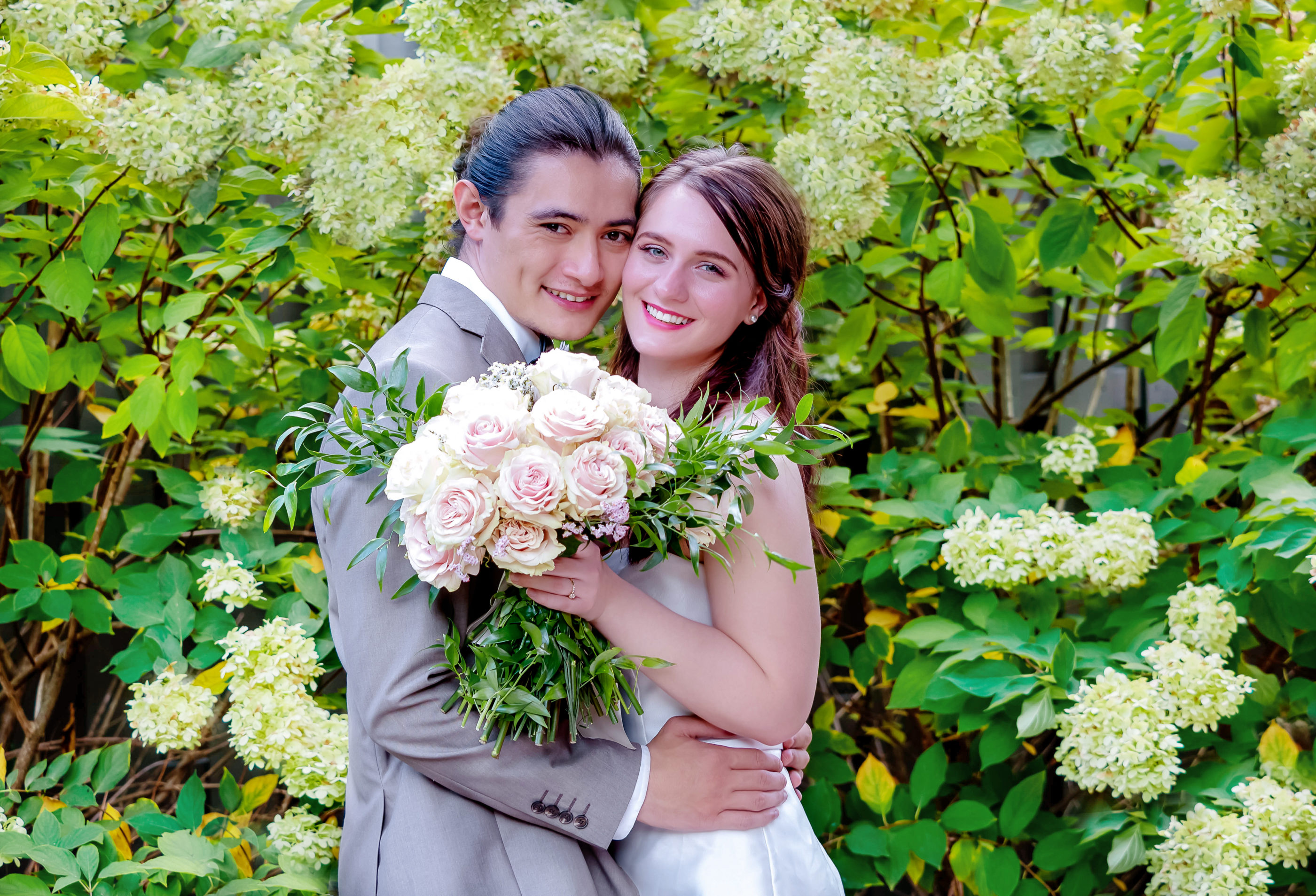 bride and groom smiling happily in front of white hydrangeas