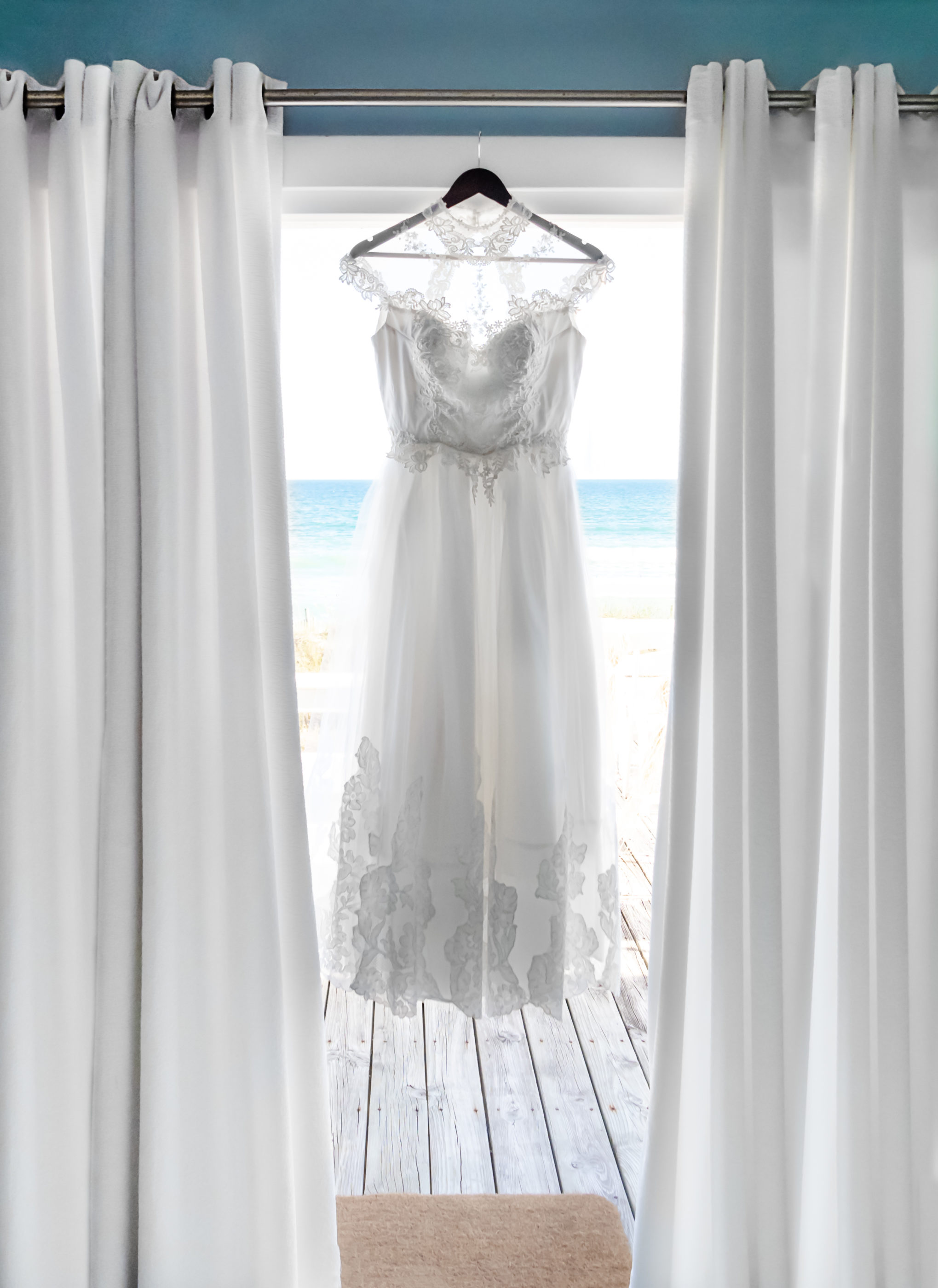 white wedding dress hanging in doorway with ocean behind