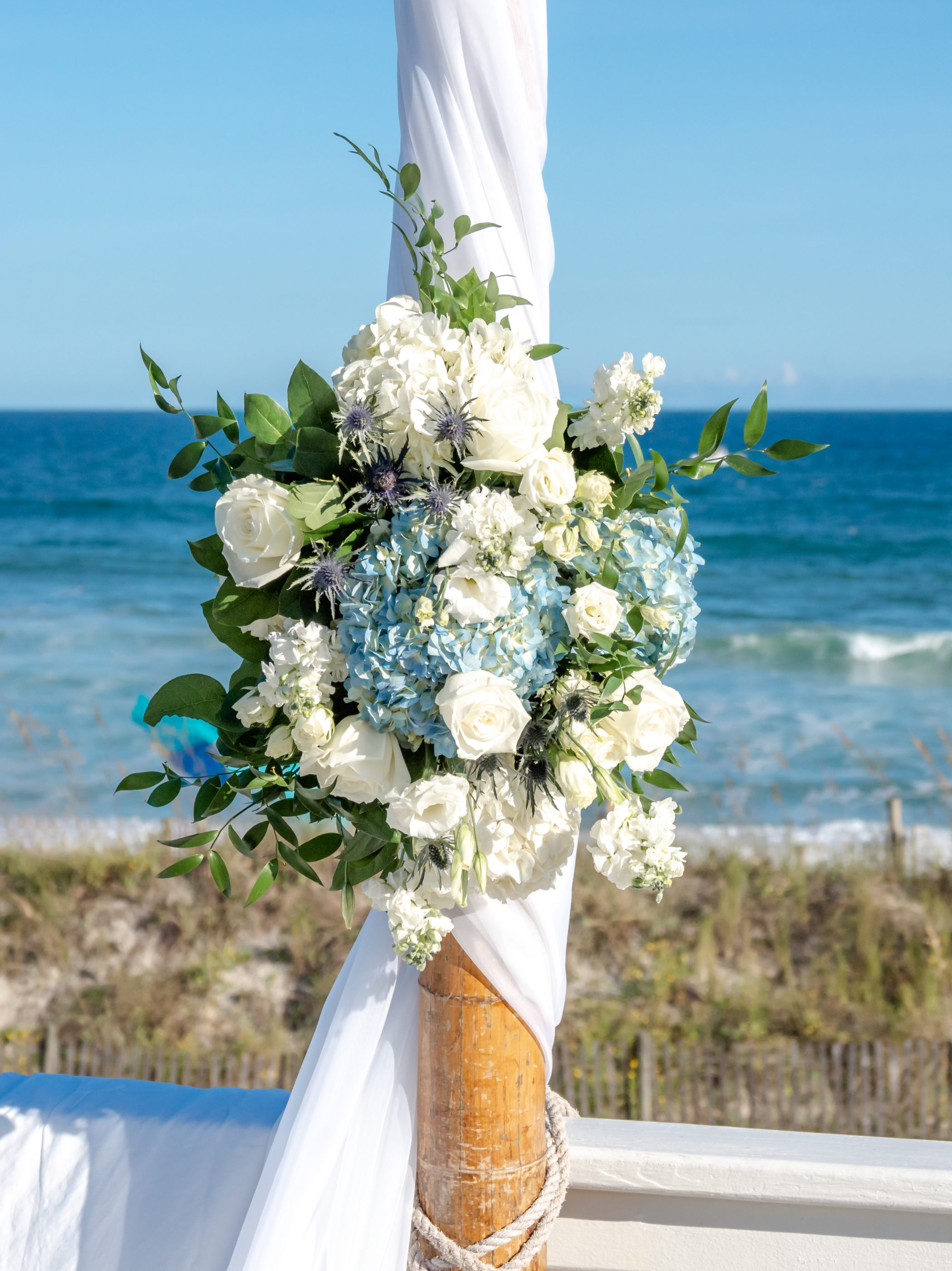 Blue hydrangeas and white roses with greenery at the center of a bamboo arch.