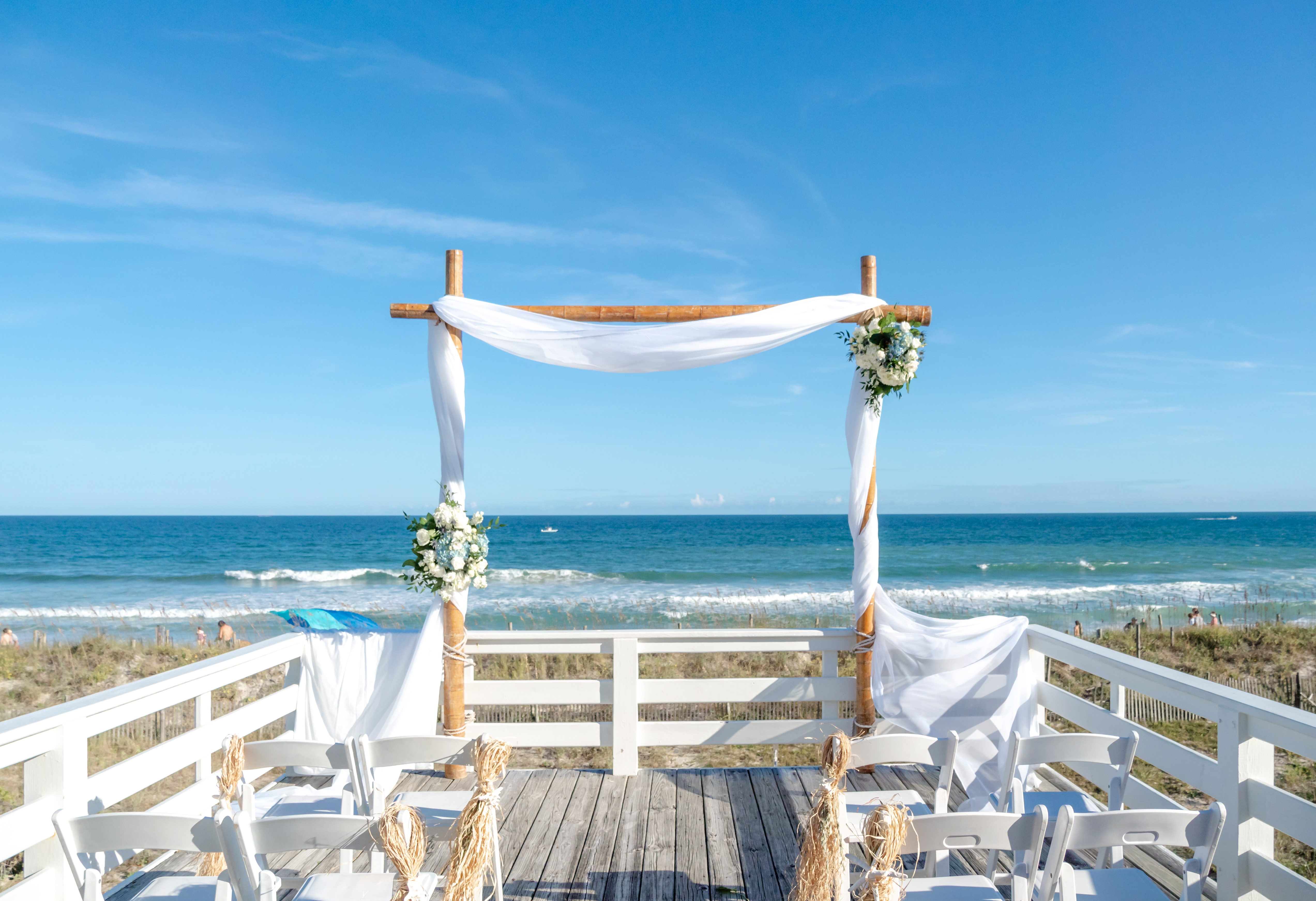 Wedding ceremony set up on a wooden deck in front of the ocean with blue hydrangeas and white roses.