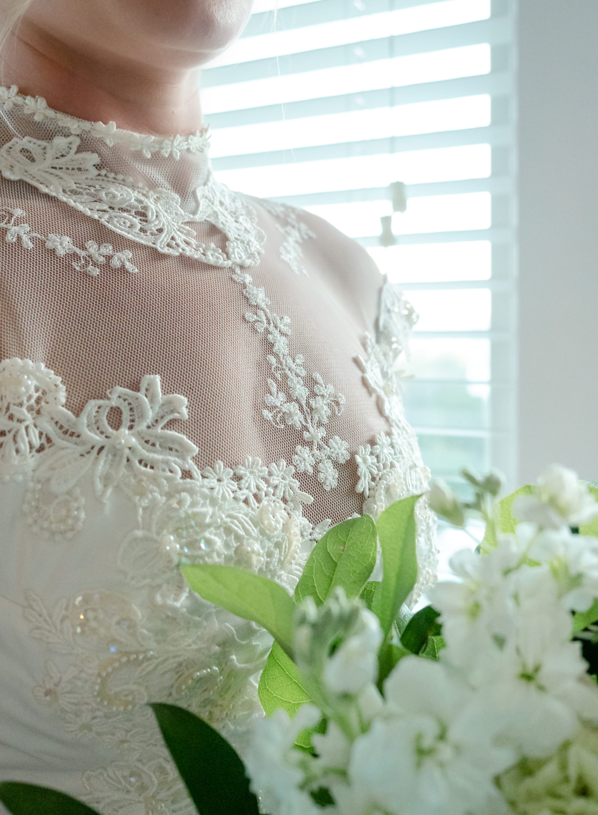 brides bodice details with her bouquet in front of the window