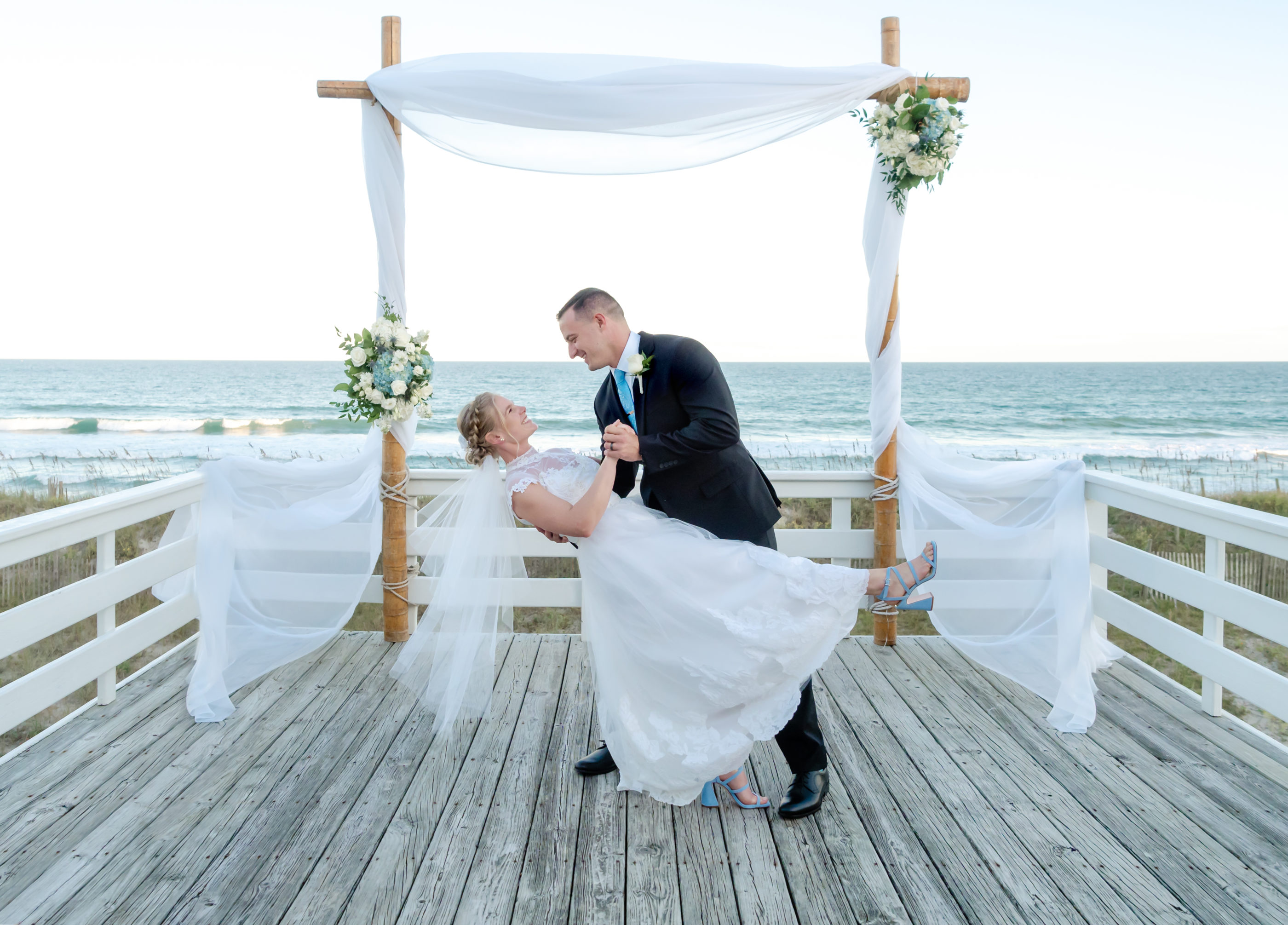 Groom dipping bride on a deck at the beach.