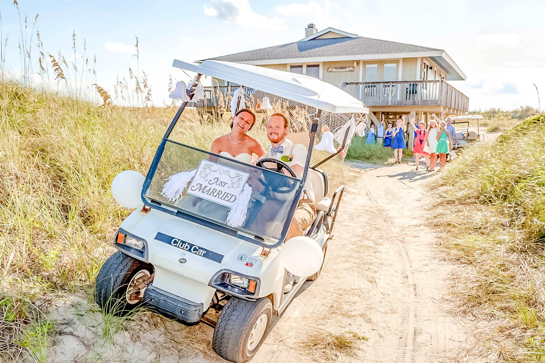 bride and groom in a golf cart with a just married sign leaving the ceremony with guests waving goodbye