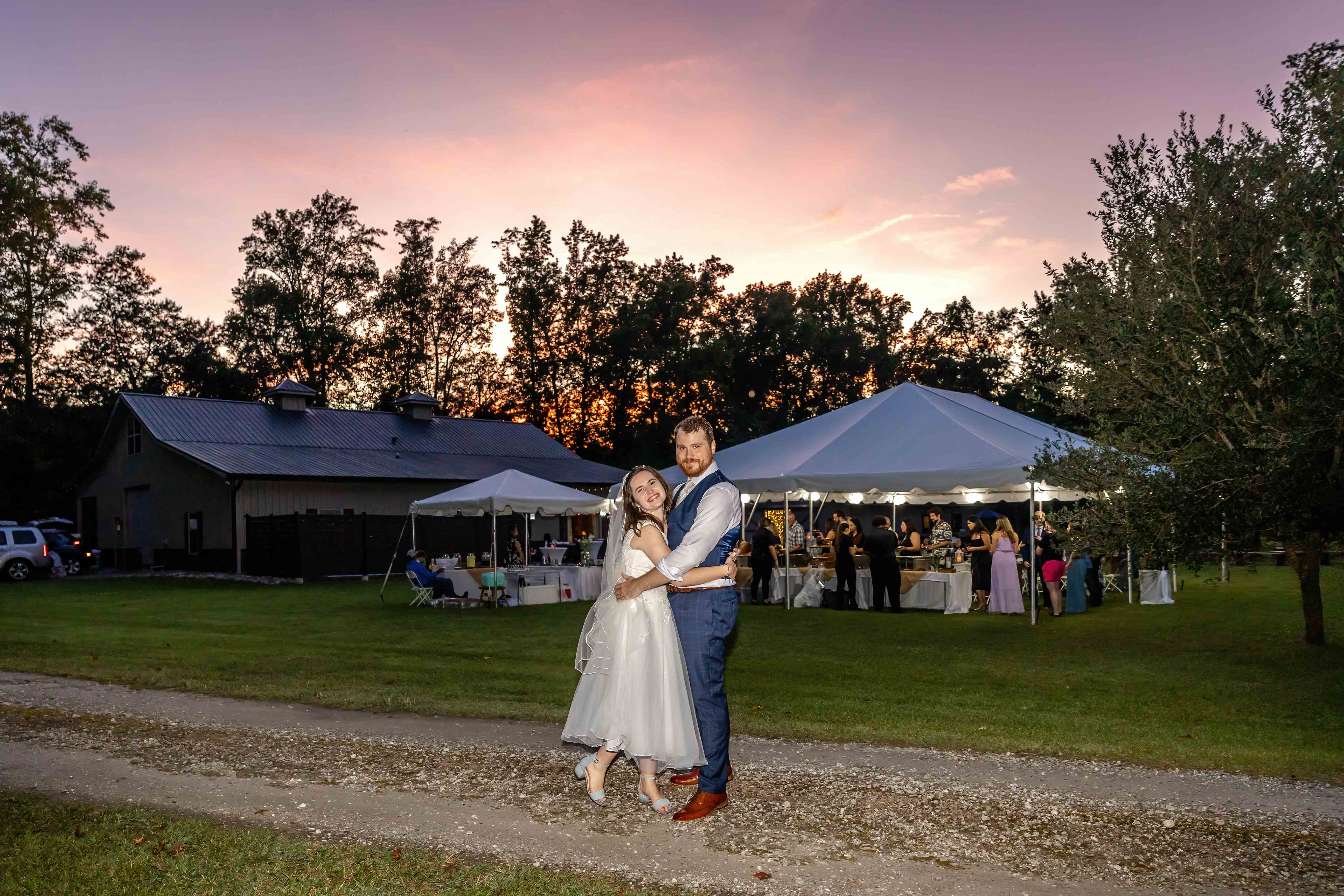 Bride and groom embrace with a beautiful sunset sky in the background at their outdoor wedding.