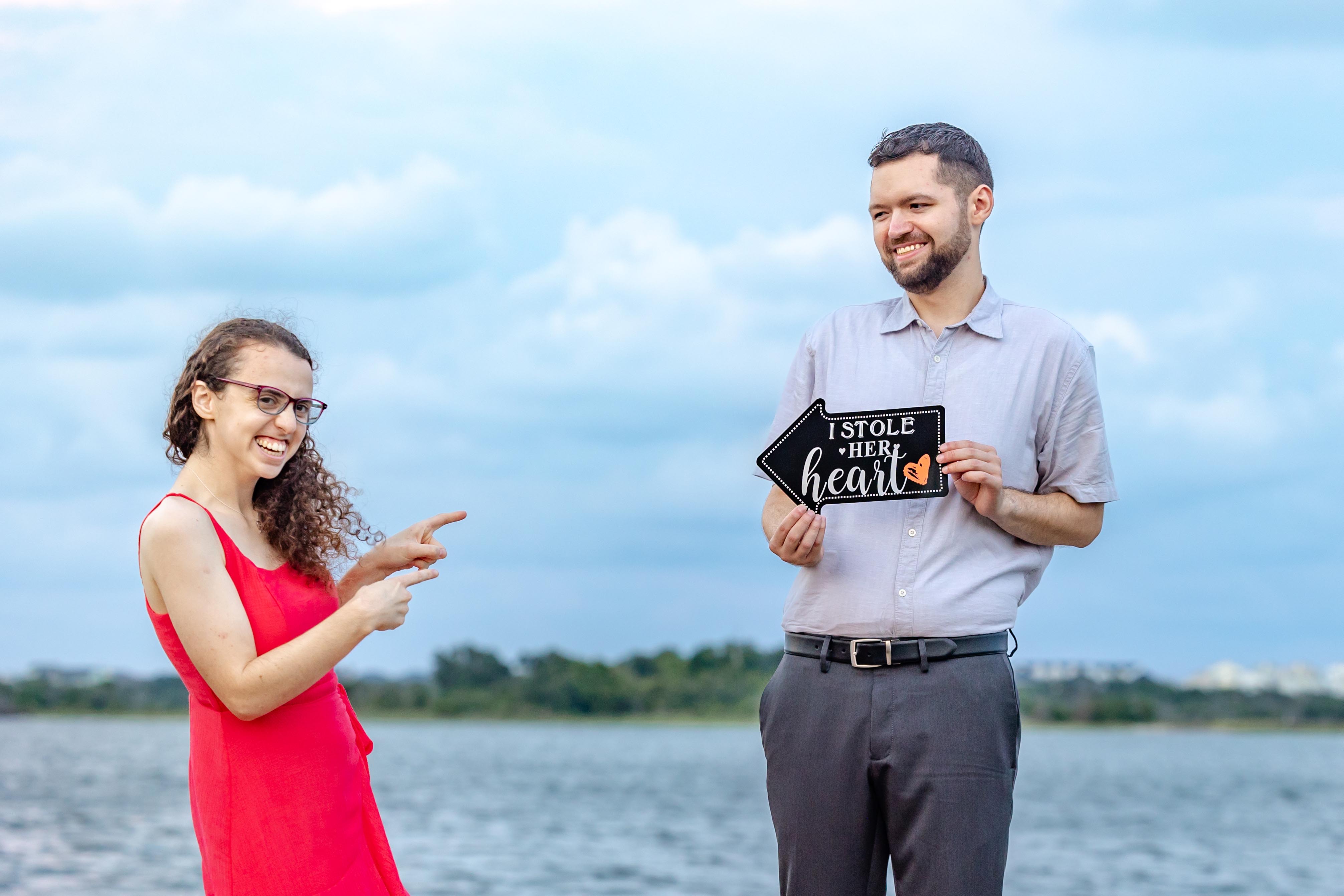 A couple poses playfully with an "I Stole Her Heart" sign, pointing at each other and smiling.