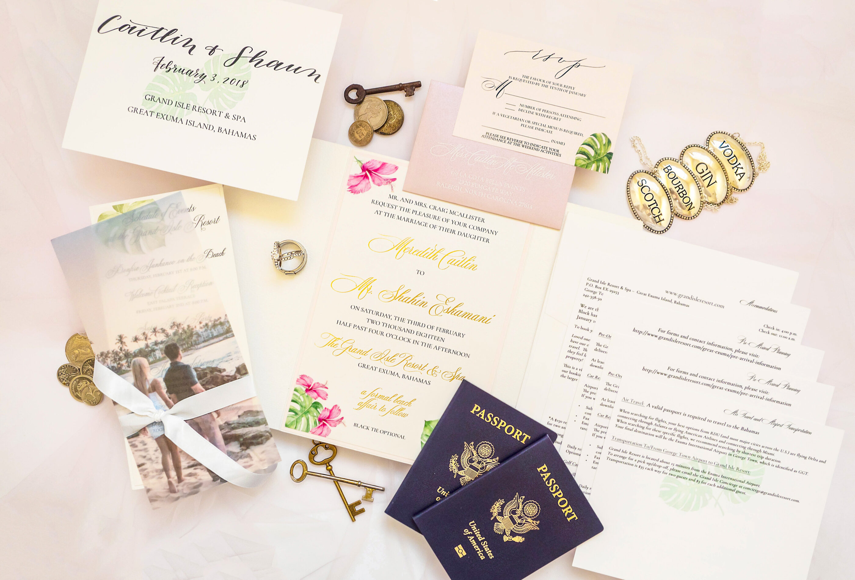 Flat lay of a tropical destination wedding invitation suite featuring multiple cards, gold keys, vintage coins, wedding rings, and two U.S. passports, styled with soft pink and floral accents for a beach wedding in the Bahamas.
