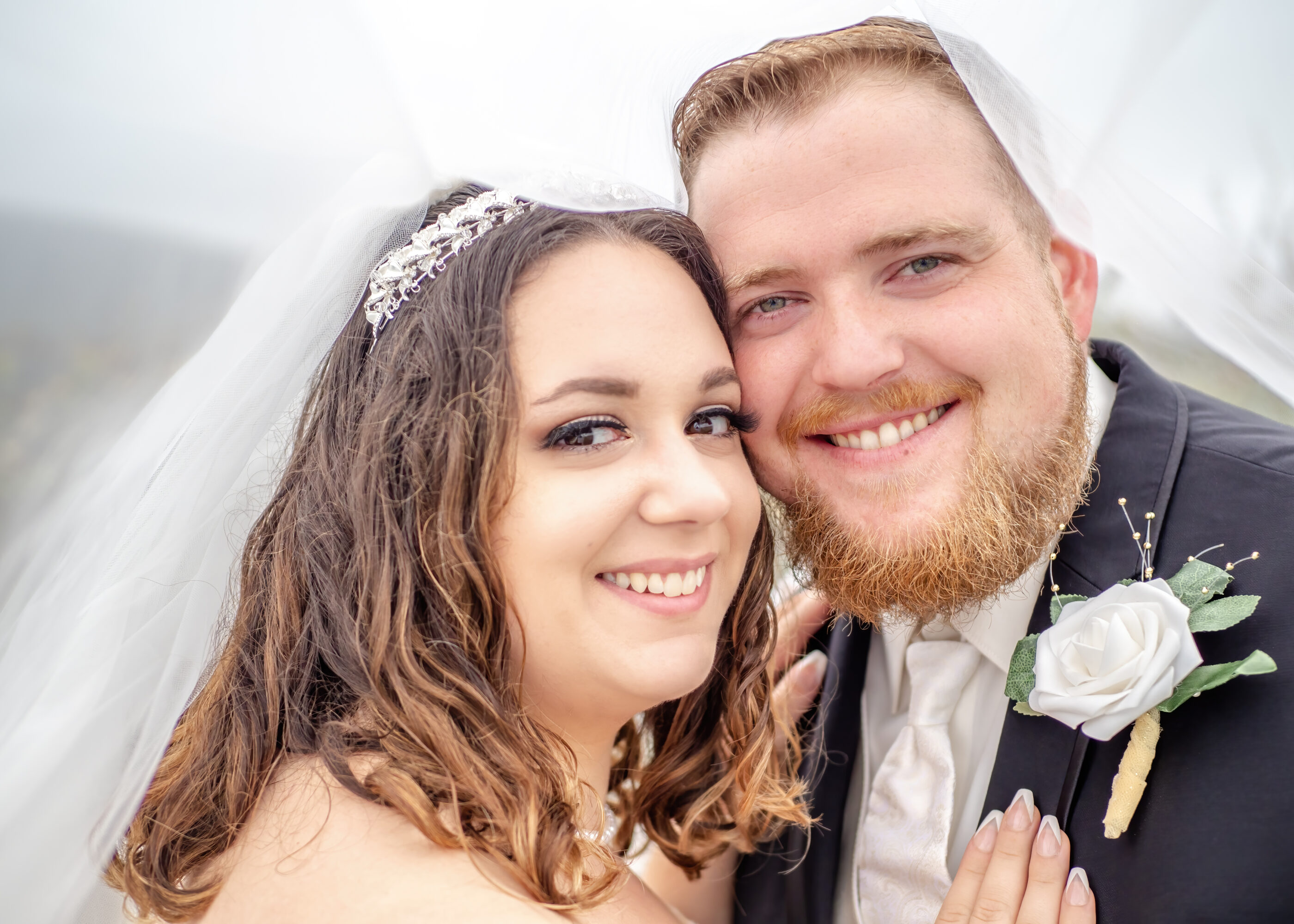 Close-up of bride and groom smiling beneath a sheer wedding veil.