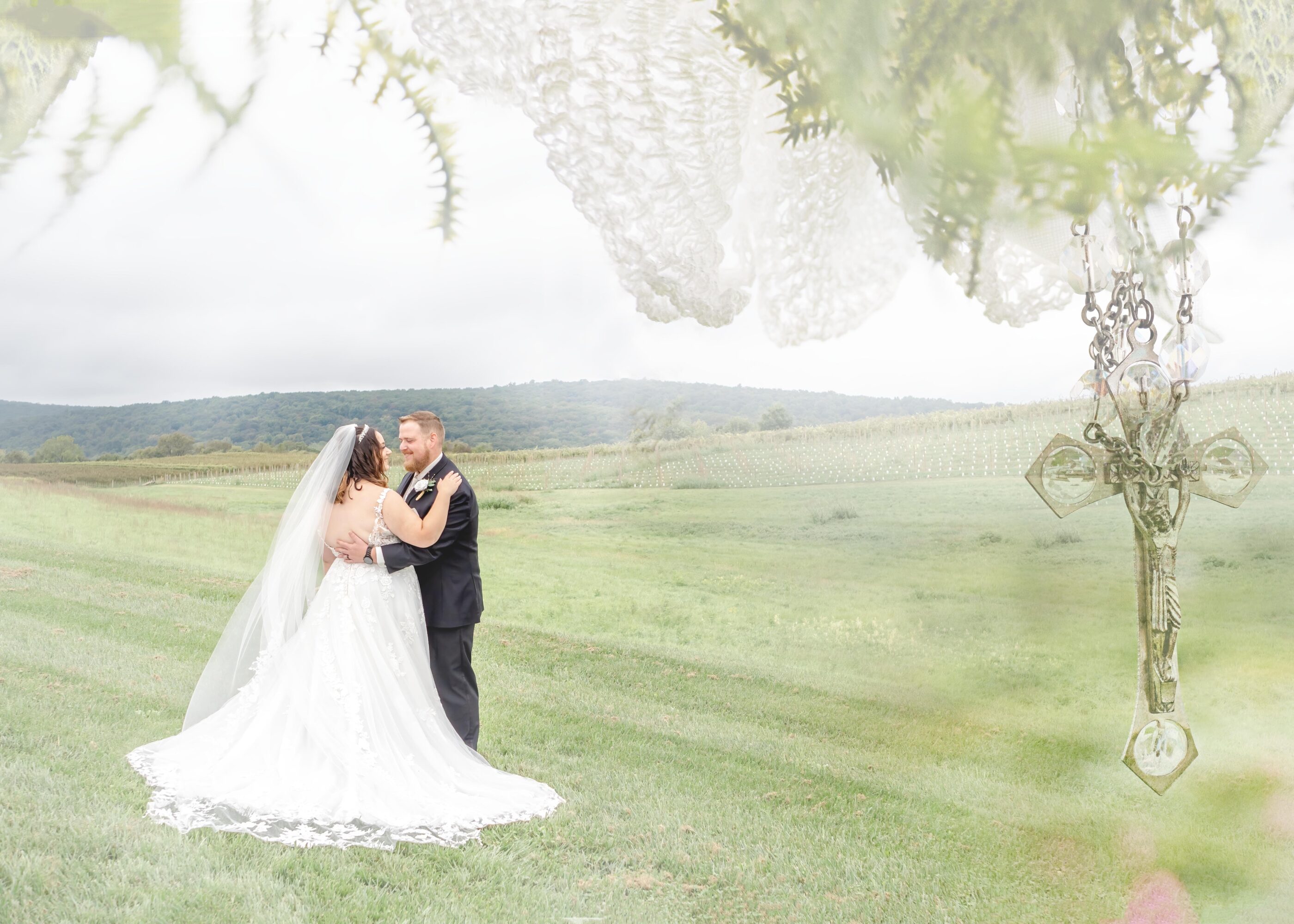 Bride and groom in vineyard embrace with a transparent overlay of a rosary cross and veil.